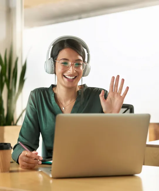 Business woman waves on a video call with headphones.